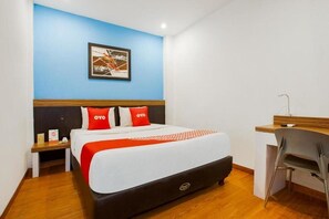 A hotel room with a bed, a desk, a chair, and a picture on the wall.