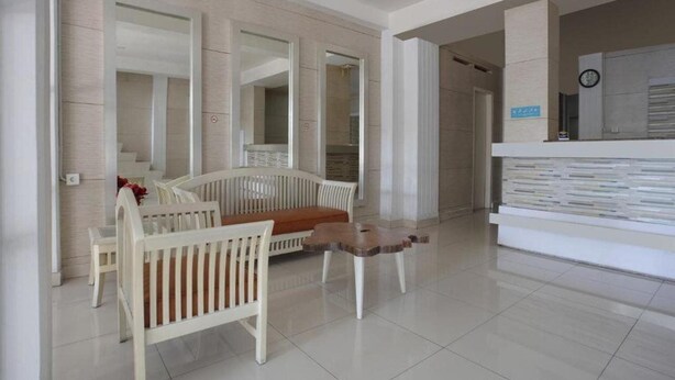 A modern living room with a white sofa, a wooden coffee table, and a white cabinet with books. - OYO 3743 Gania Hotel (Bandung)