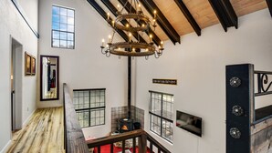 Une pièce spacieuse avec un plafond haut, un escalier en bois, une cheminée et un lustre.