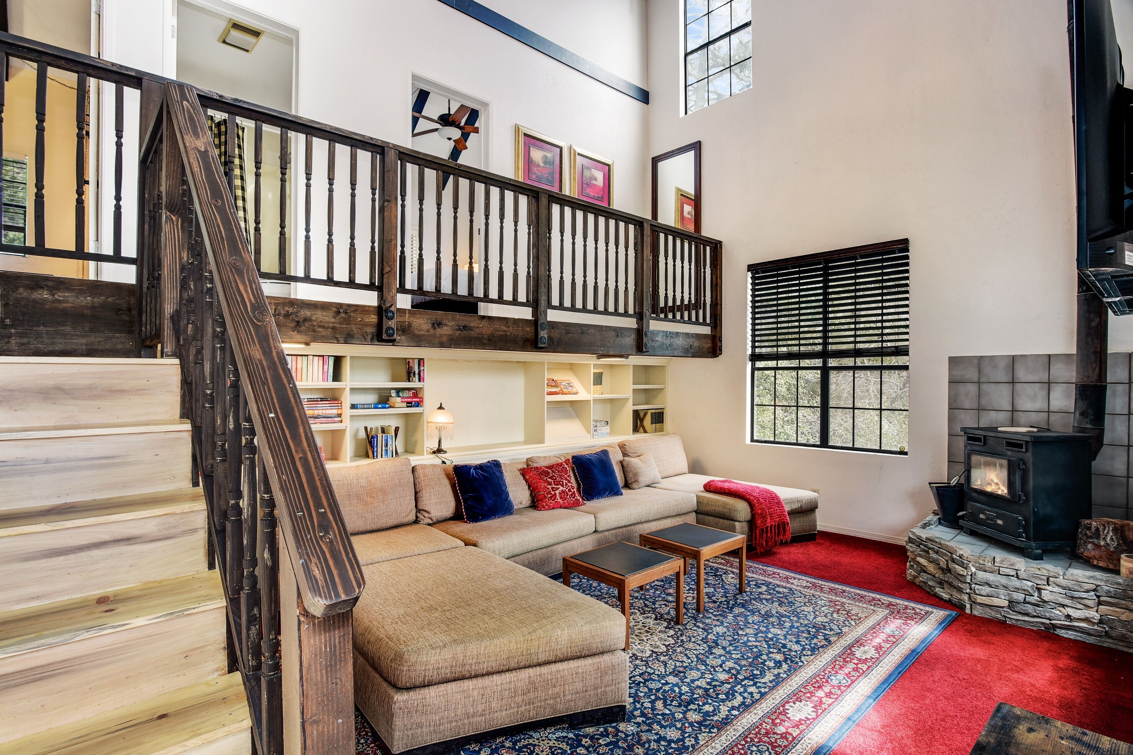 A spacious living room with a high ceiling, a wooden staircase, a built-in fireplace, and a large window.