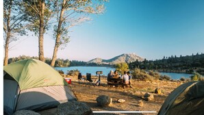 Une scène de camping avec des tentes, une table de pique-nique et un lac.