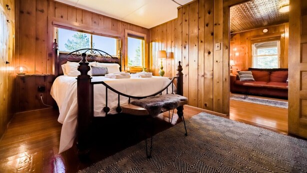 Une chambre aménagée dans une cabane en bois, avec un lit, un banc et une vue sur l’extérieur.