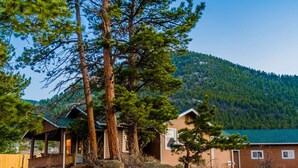 Une cabane dotée d’une véranda et d’un petit bâtiment attenant, entourée d’arbres et avec une montagne en toile de fond.
