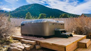 Un bain à remous doté d’une terrasse en bois et d’escaliers, entouré d’une clôture en bois et avec une montagne en arrière-plan.