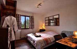 Un dormitorio con cama, cómoda, espejo, ventana con cortinas y una mesa con lámpara.