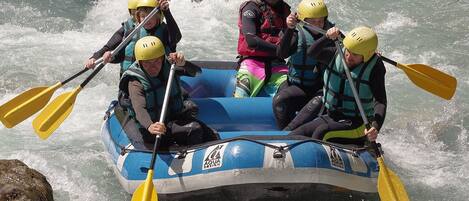A group of people in a blue inflatable raft with yellow paddles, navigating through a river.