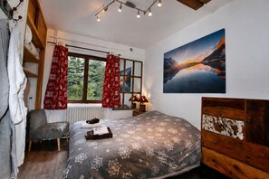 A bedroom with a bed, a chair, a window with curtains, a radiator, a painting, and a wooden dresser.