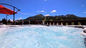 A hot tub with a mountain view, a red umbrella, and a glass of wine.