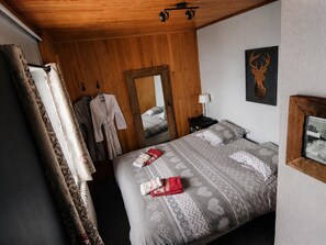 A bedroom with a wooden ceiling, a bed with patterned bedding, a nightstand with a lamp, and a deer head decoration on the wall. - CHALET FOR 16–18 PEOPLE WITH JACUZZI, SAUNA, MOVIE ROOM, AND VIEWS OF THE SLOPES AND MOUNTAINS (Montgenèvre)