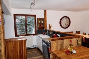 A kitchen with wooden cabinets, a built-in oven, and a window with a view of snow-covered trees. - CHALET FOR 16–18 PEOPLE WITH JACUZZI, SAUNA, MOVIE ROOM, AND VIEWS OF THE SLOPES AND MOUNTAINS (Montgenèvre)