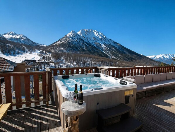 A hot tub with a mountain view, wooden deck, and outdoor seating.