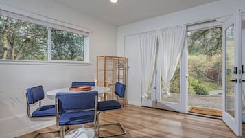 Une pièce avec une table ronde, quatre chaises bleues, une chaise en bois et une fenêtre avec des rideaux.
