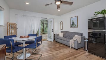 Un salon moderne comprenant un coin repas, un canapé gris, un ventilateur de plafond et un réfrigérateur noir.