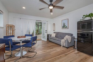 Un salon moderne comprenant un coin repas, un canapé gris, un ventilateur de plafond et un réfrigérateur noir.