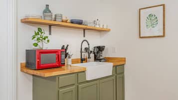 Une cuisine avec un micro-ondes rouge, un évier et une étagère en bois au-dessus, où sont rangés divers plats et une plante.