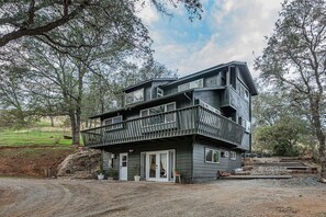 Une maison moderne à deux étages, dotée d’un balcon, entourée d’arbres et bordée d’une allée en gravier.