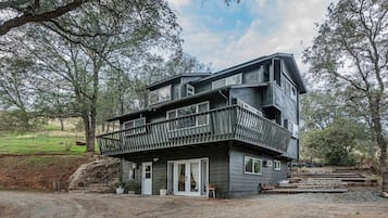 Un bâtiment à deux étages doté d’un balcon, entouré d’arbres et bordé d’une allée en gravier.