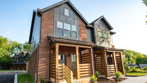 A modern two-story house with a brick facade, large windows, and a wooden porch.