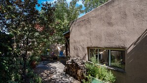 A rustic house with a thatched roof, a stone wall, and a garden with various plants and a wooden bench.