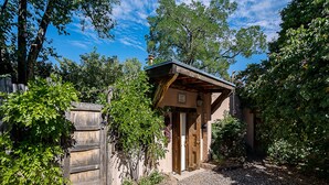 A rustic wooden building with a sloped roof, surrounded by trees and gravel.