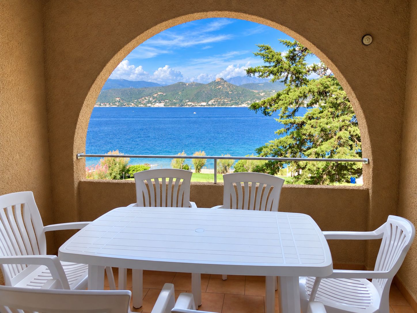 A white table and chairs set against a scenic view of a blue sea and green hills.