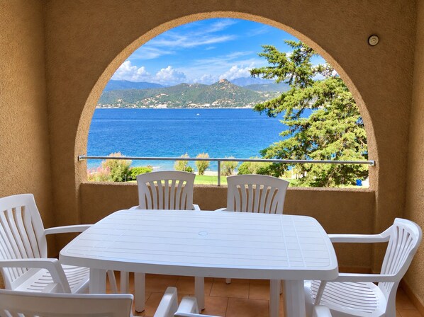A white table and chairs set against a scenic view of a blue sea and green hills.