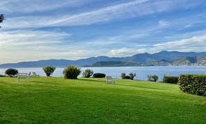 Un espace verdoyant avec un banc et une chaise, donnant sur un lac dont les montagnes se dressent à l’horizon.