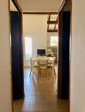 A hallway leading to a dining area with a table and chairs, a television, and a window with natural light. - Appartement vue mer et Montagne, à Létage (Calcatoggio)