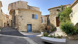 Une rue étroite bordée d’immeubles en pierre, avec une porte bleue et un banc.