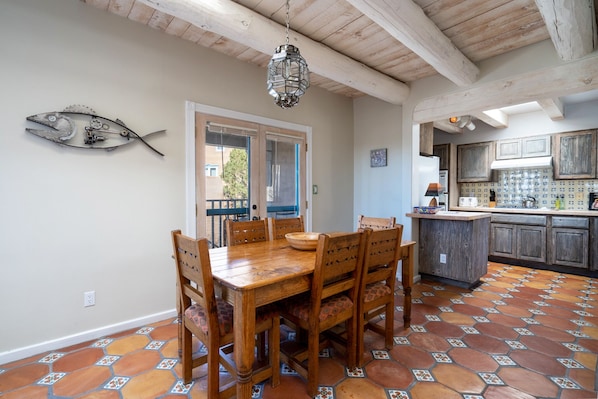 Un coin repas avec une table et des chaises en bois, une décoration murale représentant des poissons et une cuisine avec des placards en bois.