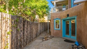 Une cour avec un chemin en pierre, une clôture en bois et un bâtiment aux portes et fenêtres turquoise.