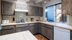 Une cuisine avec des meubles de rangement en bois, un pare-feu en carrelage, une fenêtre avec des stores et un lave-vaisselle.
