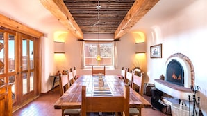 A dining area with a wooden table and chairs, a fireplace, and a window with a view. - City Views at Alma Compound | Great Location! (Santa Fe)