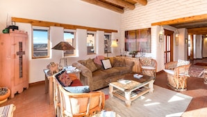 A cozy living room with a wooden ceiling, a brown sofa, a coffee table, and wicker chairs. - City Views at Alma Compound | Great Location! (Santa Fe)