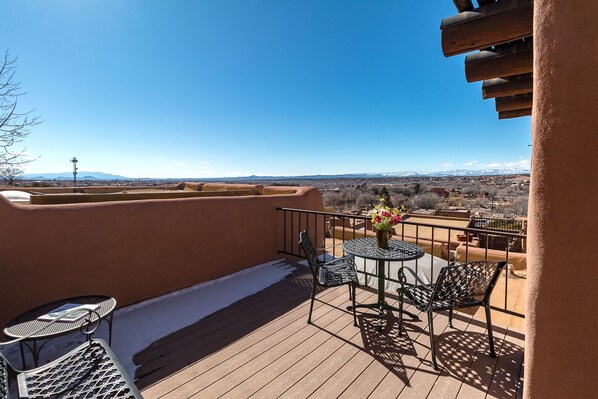 A balcony with a wooden deck, metal chairs, a small round table, and a potted plant. - City Views at Alma Compound | Great Location! (Santa Fe)
