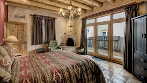 A bedroom with a large bed, a wooden ceiling, a fireplace, and a view through a glass door.