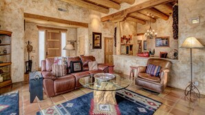 A spacious living room with a leather sofa, a glass coffee table, and a rustic stone fireplace.