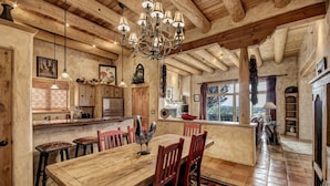 A rustic kitchen with wooden beams, a large wooden dining table, and a chandelier.