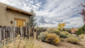 A rustic building with a wooden door, surrounded by a wooden fence and various desert plants.