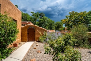 A traditional adobe building with a curved entrance, surrounded by gravel and plants.