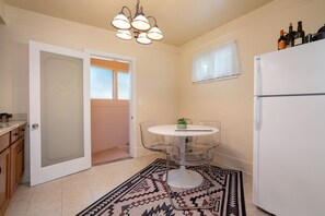 A compact kitchen with a white refrigerator, a dining table with chairs, and a patterned rug.