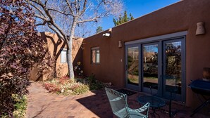 A patio with a metal chair and table, a brick pathway, and a building with a brown exterior and glass doors. - Puertas de Canyon Road | Patio, Fenced Yard! (Santa Fe)
