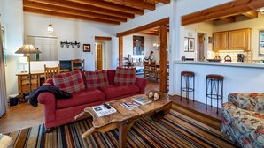 A cozy living room with a red sofa, wooden coffee table, and striped rug. - Puertas de Canyon Road | Patio, Fenced Yard! (Santa Fe)