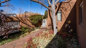 A courtyard with a brick pathway, a tree, and a building with a window. - Puertas de Canyon Road | Patio, Fenced Yard! (Santa Fe)