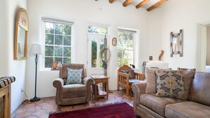 Un salon chaleureux avec un canapé en cuir, une chaise en bois, un tapis rouge et de grandes fenêtres donnant sur un paysage verdoyant.