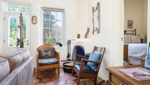 Une pièce chaleureuse avec un fauteuil à bascule en bois, un fauteuil rembourré et un canapé. Une fenêtre offre une vue sur la verdure environnante.