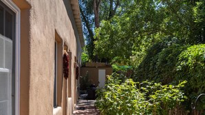 Un étroit sentier mène à un bâtiment à la façade beige, entouré d’une végétation luxuriante et d’arbres.