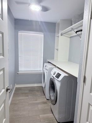 A laundry room with a washing machine, a dryer, a ceiling fan, and a window with blinds. - 3-bedroom house in North Laredo with AC, WiFi kitchen equipped (Laredo)