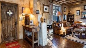 A rustic interior with exposed wooden beams, a leather sofa, a coffee table, and a traditional lamp. - Western Cowboy | Luxe Design, Four Fireplaces + Close to Plaza! (Santa Fe)