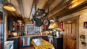A rustic kitchen with wooden beams, a central island table, and various kitchen appliances. - Western Cowboy | Luxe Design, Four Fireplaces + Close to Plaza! (Santa Fe)